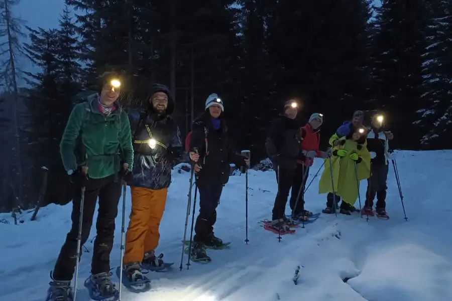 Gruppo di escursionisti con lampade frontali durante una ciaspolata notturna tra i boschi innevati delle Dolomiti con WeHike